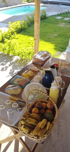 A breakfast setup with various food items and drinks on a table outdoors, near a pool. - Pousada Al Mare (Cajueiro da Praia)