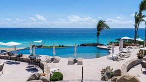 A poolside area with lounge chairs and umbrellas, a clear view of the ocean, and a stone pathway leading to the pool.