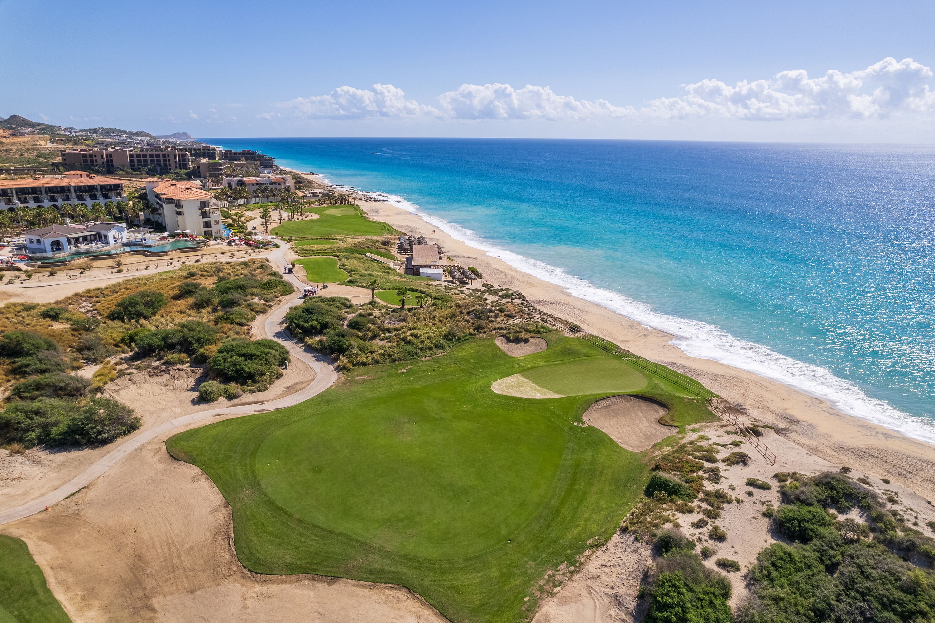 A coastal golf course with a beach and ocean views, surrounded by buildings and greenery.