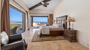 A bedroom with a large bed, a dresser, and a view of the ocean.