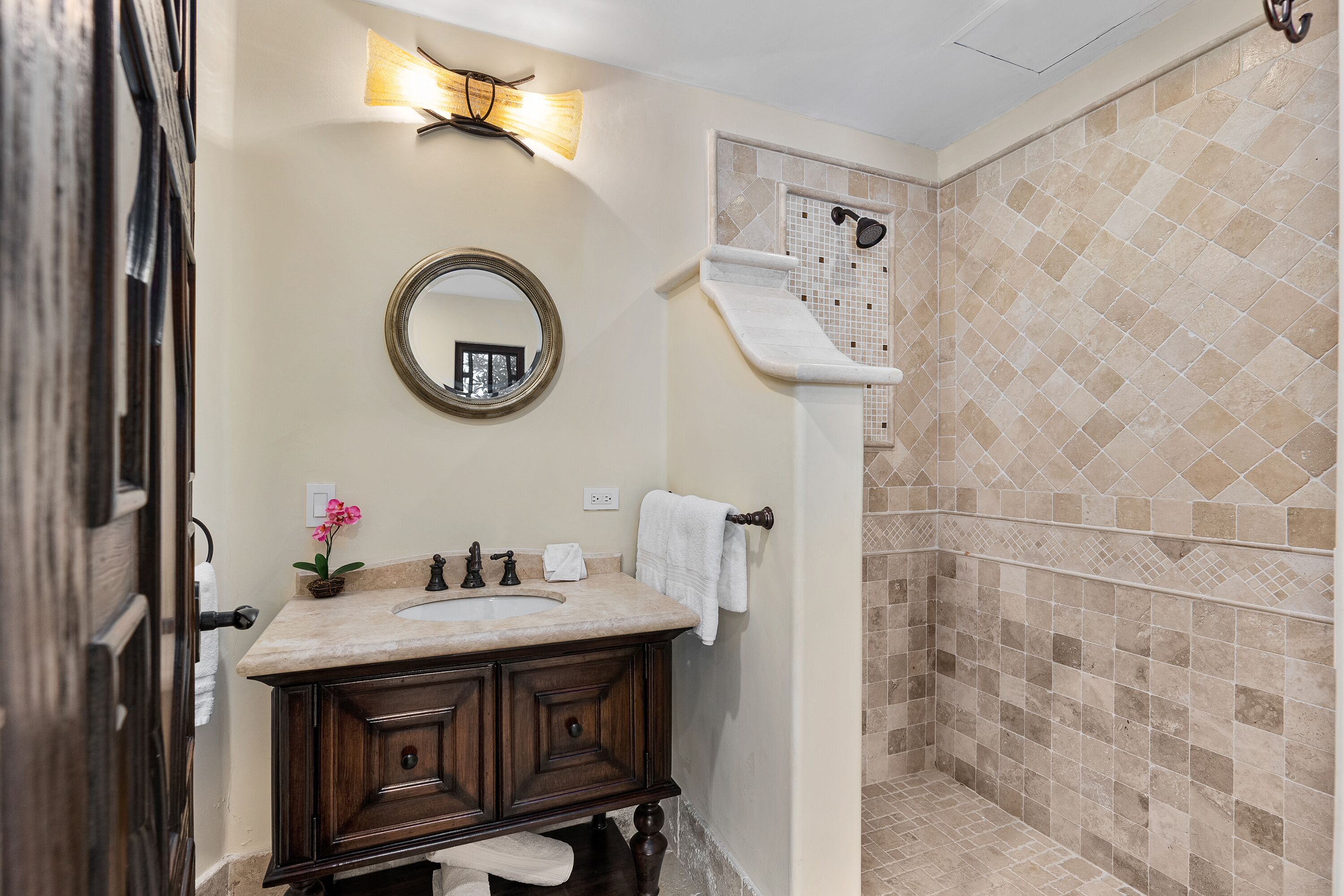A bathroom with a vanity, a mirror, a towel rack, and a shower area with tiled walls.