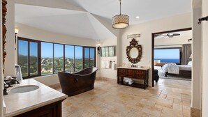 A spacious bathroom with a large bathtub, a vanity with a mirror, and a view of the landscape through large windows.