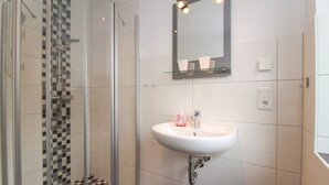 A bathroom with a glass-enclosed shower, a white sink with a mirror above it, and a checkered floor pattern. - Bright, modern ground floor apartment for 4 people including four-legged friends (Norden)