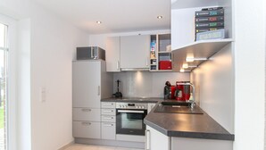 A modern kitchen with white cabinets, a built-in oven, a microwave, and a coffee machine. - Bright, modern ground floor apartment for 4 people including four-legged friends (Norden)
