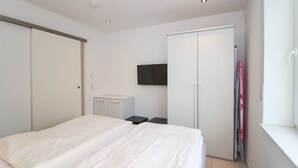 A bedroom with a bed, a wardrobe, a TV, and a window. - Bright, modern ground floor apartment for 4 people including four-legged friends (Norden)