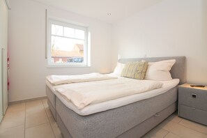 Een slaapkamer met een bed, kussens, een nachtkastje en een raam.