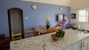 A kitchen with a marble countertop, wooden chairs, a dining table, and a potted orchid. - Timeless - Lovely beach cottage. Private pool, ocean view, beach access. R &R ! (Kingston)