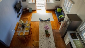 A spacious kitchen with wooden flooring, a central island with a vase of flowers, and a dining area with wooden chairs and yellow plates. - Timeless - Lovely beach cottage. Private pool, ocean view, beach access. R &R ! (Kingston)