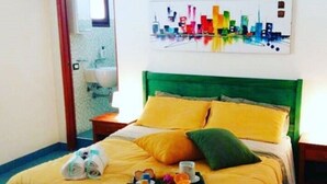 A hotel room with a green headboard, yellow bedding, and a cityscape painting on the wall. - Apollo's Terraces-Beach apartments less than 20 m from the sea! Levant (Marinella)