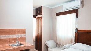 A hotel room with a wooden cabinet, a sink, a chair, a bed, and an air conditioning unit. - Apartahotel Dubai (Punta Cana)