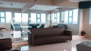 A modern office space with a glass partition, a brown leather sofa, and a conference table with chairs. - Apartahotel Dubai (Punta Cana)