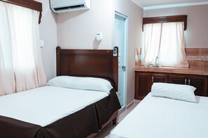 A hotel room with two single beds, a wooden headboard, a bathroom with a shower, and a small kitchenette. - Apartahotel Dubai (Punta Cana)