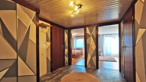 A hallway with geometric wall designs, a woven rug, and a bed visible through an open door. - Haus Rist - Apartment Panoramablick in Altstädten im Allgäu (Sonthofen)