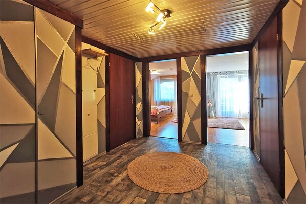 A hallway with geometric wall designs, a woven rug, and a bed visible through an open door. - Haus Rist - Apartment Panoramablick in Altstädten im Allgäu (Sonthofen)