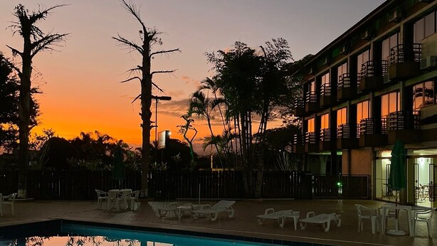 A swimming pool with lounge chairs, surrounded by trees and a building with balconies. - Hotel Canto da Ilha (Florianópolis)