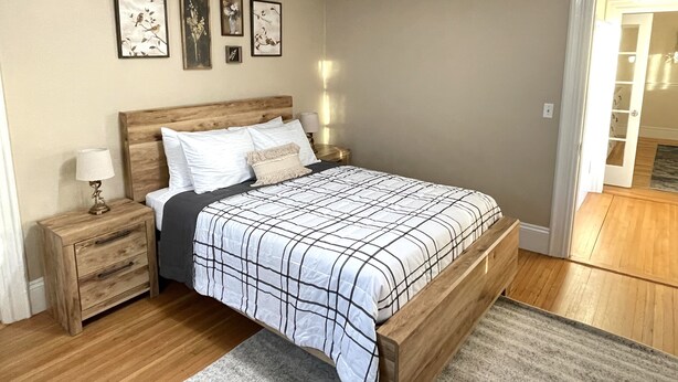 Ein Schlafzimmer mit einem hölzernen Bett, Nachttischen, einem Nachtschränkchen und einer Tür zu einem Flur.