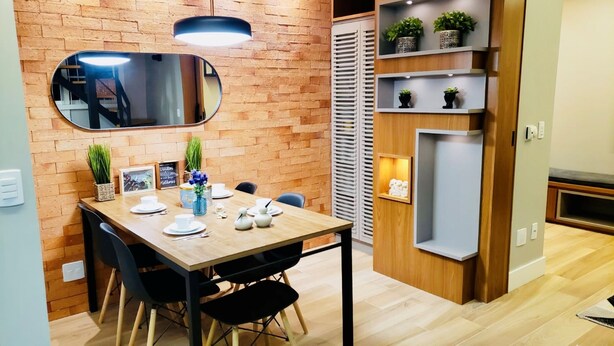 A dining area with a brick wall, a mirror, and shelves with plants.
