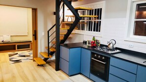 A modern kitchen with blue cabinets, a black stove, and a wooden staircase.