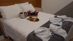 A neatly made bed with white linens, a fruit platter, a bottle of water, and a glass of wine on the bed.