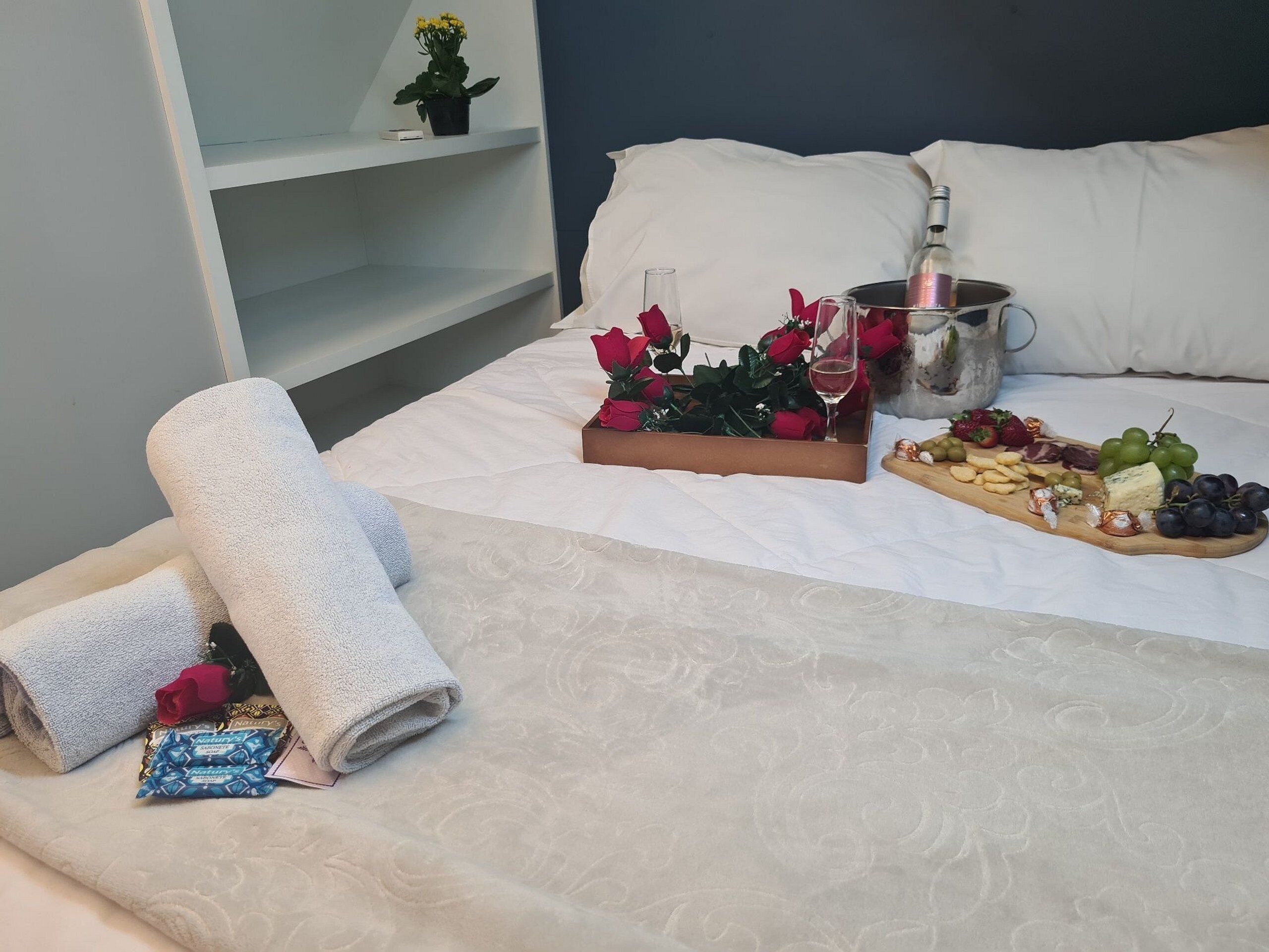 A neatly made bed with a tray of snacks, a bottle of wine, and a bouquet of roses.