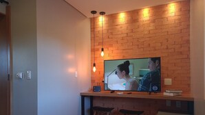 A modern living room with a brick wall, a flat-screen TV, two stools, and a bench.