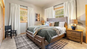 Une chambre à coucher avec un lit en bois, une table de chevet, une chaise et une fenêtre avec des rideaux.