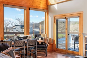 A room with a wooden ceiling, large windows, a dining area with chairs and a table, and a sliding glass door leading outside. - Luxury Vacation Cabin on the White River (Cotter)