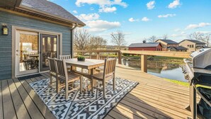 Une terrasse avec une table et des chaises, un barbecue et une vue sur un étang et des bâtiments.