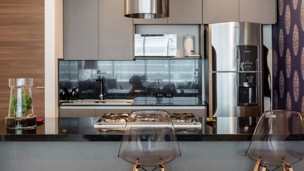Een moderne keuken met roestvrijstalen apparatuur, een glazen spatwand en een centraal eiland met krukken.