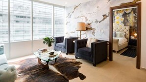 Een moderne woonkamer met een glazen salontafel, twee banken, een lamp en een muurschildering.