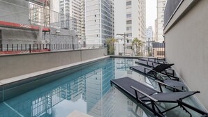 Una piscina sul tetto con lettini e vista sui grattacieli circostanti.