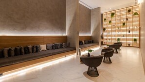 Una hall moderna con una lunga panca, un'area salotto con poltrone e una parete con mensole che espongono piante.