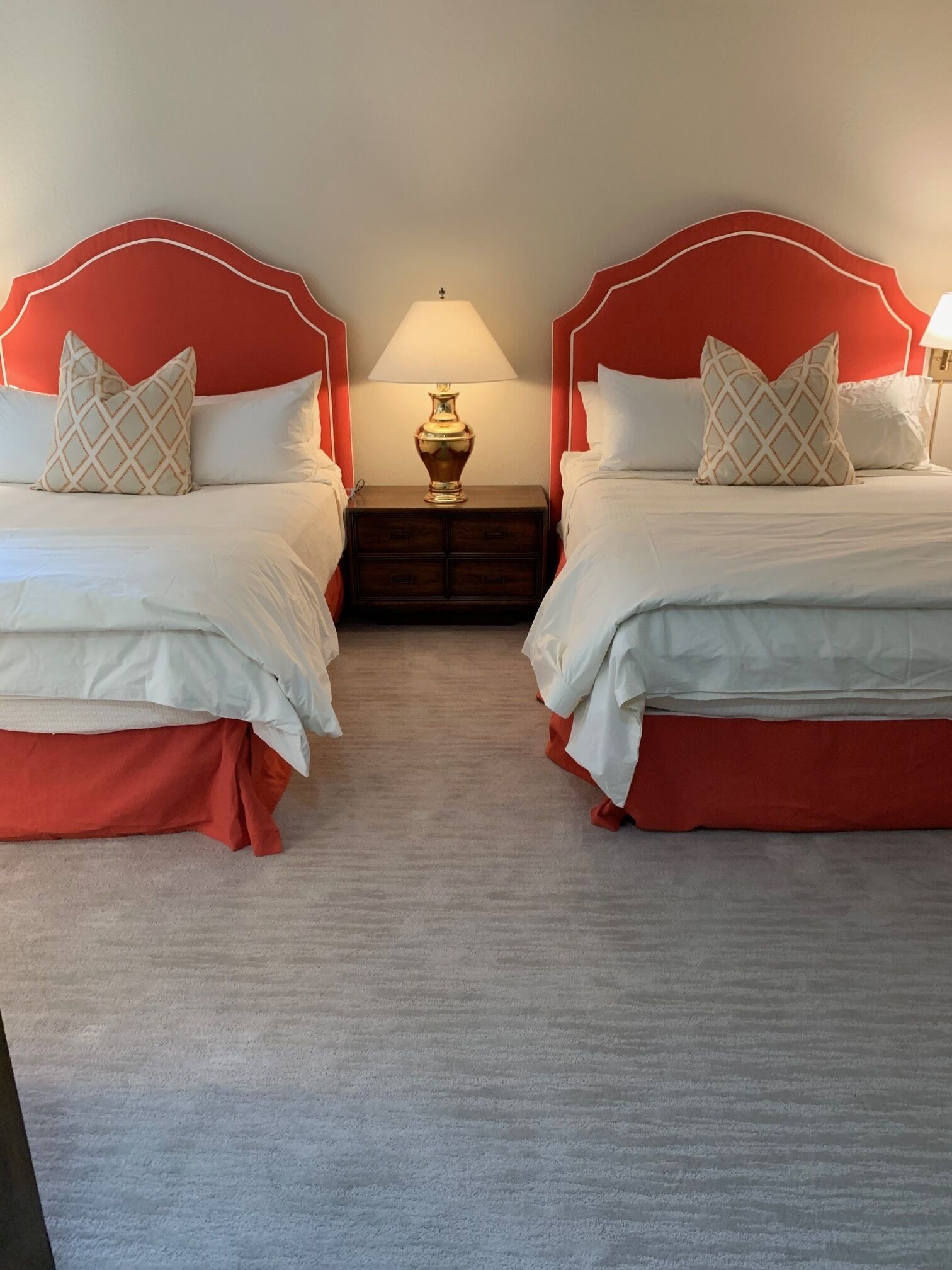 Une chambre d’hôtel avec deux lits, chacun doté d’une tête de lit rouge, de draps blancs et d’oreillers assortis. Une table de chevet avec une lampe se trouve entre les deux lits.