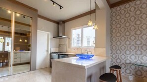 A modern kitchen with a large island, pendant lighting, and a view of the city through the window. - Tiete Classic I Stunning 3 Bedroom in Jardins (São Paulo)