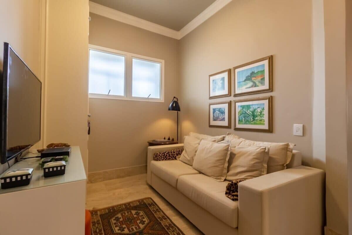 Una sala de estar con un sofá beige, un televisor de pantalla plana, una lámpara y cuadros en la pared.