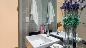 Une salle de bain moderne avec deux lavabos, un miroir et un vase rempli de fleurs de lavande.