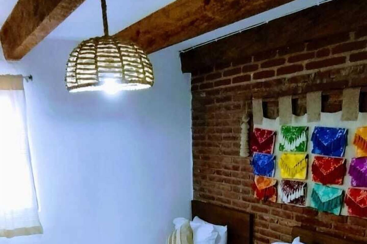 Une chambre d’hôtel avec deux lits, un mur en briques, un luminaire suspendu et une fenêtre avec des rideaux.