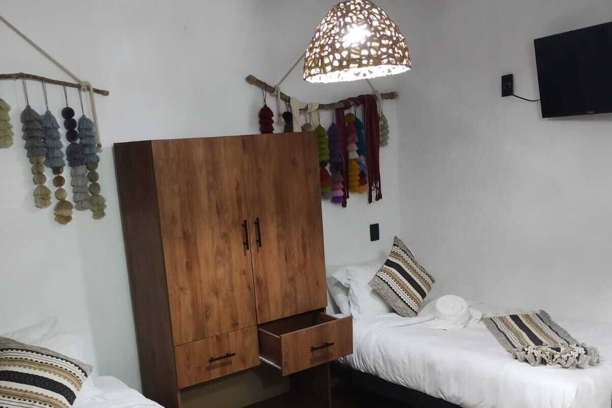 Une chambre avec deux lits, une armoire en bois, un luminaire suspendu et un téléviseur fixé au mur.