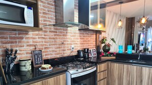 A modern kitchen with a brick wall, stainless steel appliances, wooden cabinets, and a black countertop. - Duplex 02 Suites - Cond.Fechado 08 P (Gramado)