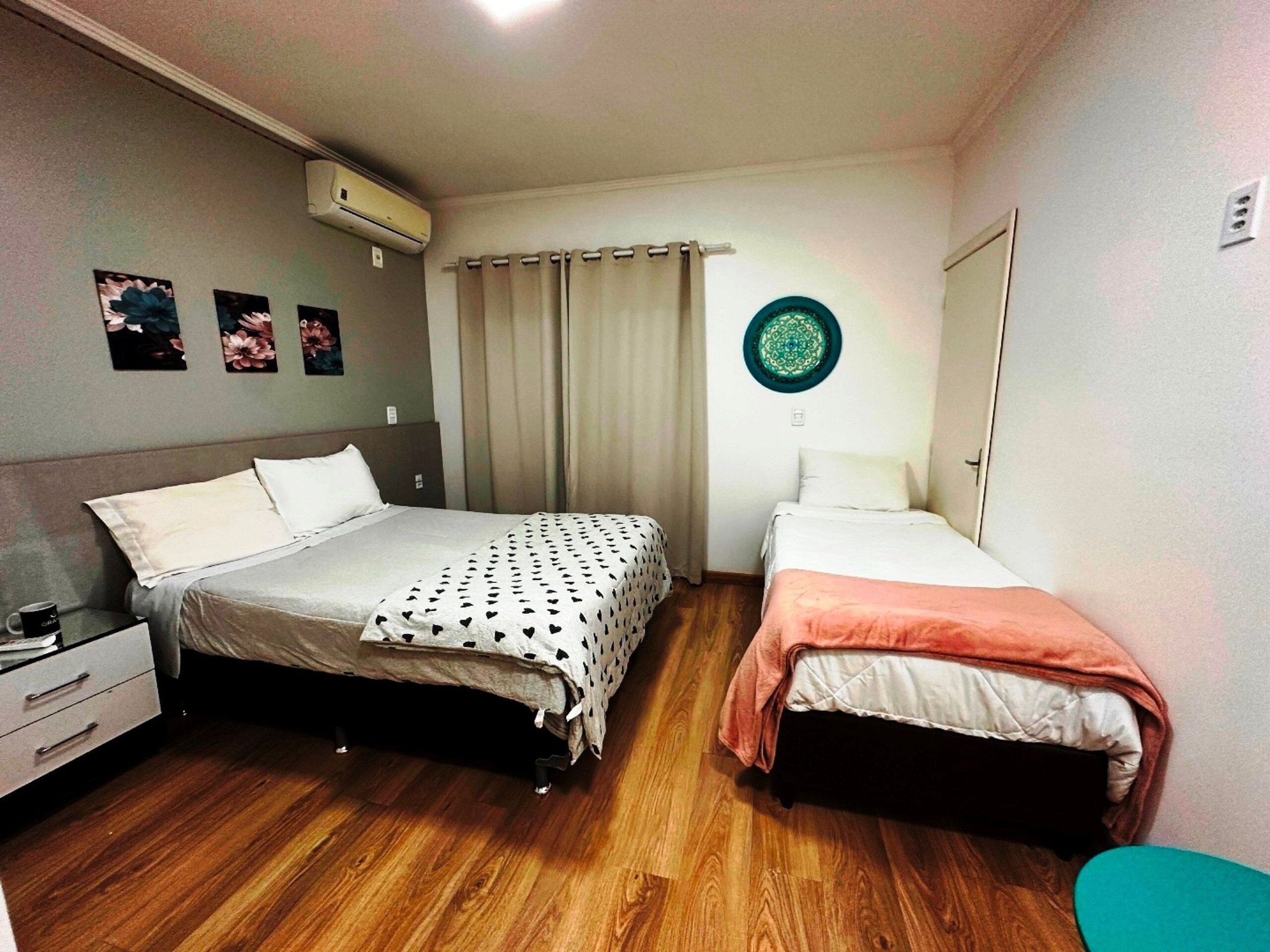 A bedroom with two beds, a wooden floor, a wall-mounted air conditioner, and a door.