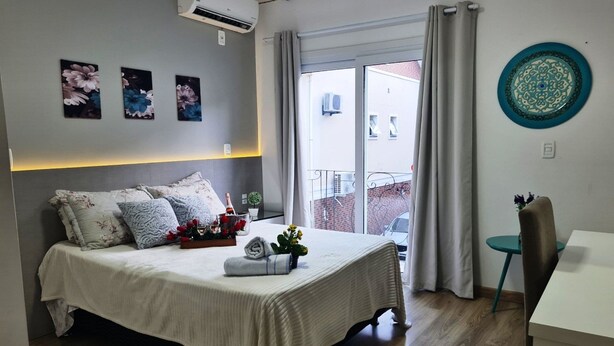 A bedroom with a bed, a bedside table, a chair, a window with curtains, and wall art. - Duplex 02 Suites - Cond.Fechado 08 P (Gramado)