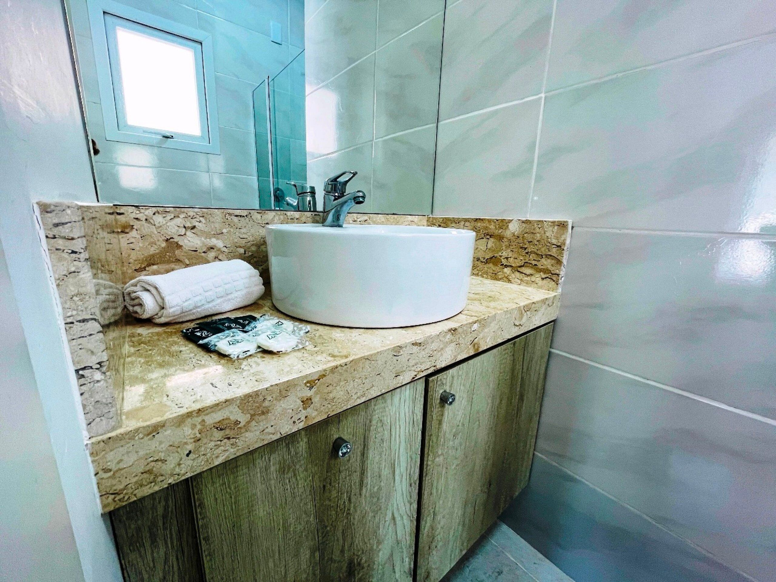 Un baño con encimera de mármol, lavamanos blanco, una toalla y una botella de jabón para manos.