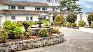 A two-story house with a stone fountain in the front yard, surrounded by various shrubs and a stone wall. - Sparkling Clean, Private & Quiet! Amazing Ocean Views [7] (Brookings)