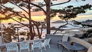 A terrace with white metal chairs and a table, overlooking a beach with rocks and a sunset. - Sparkling Clean, Private & Quiet! Amazing Ocean Views [7] (Brookings)