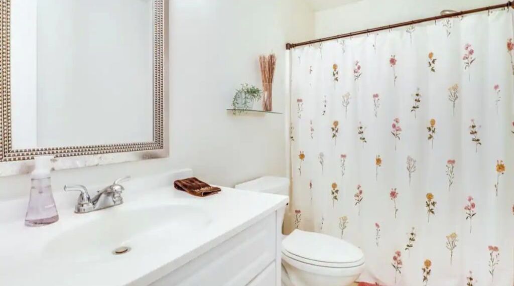 Un baño con lavamanos blanco, un espejo, un inodoro y una cortina de ducha con estampado floral.