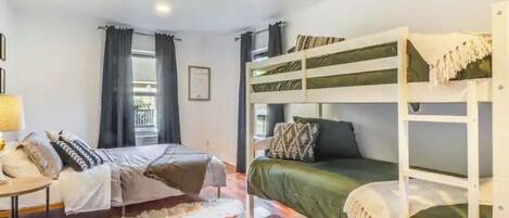 Habitación con literas, un escritorio, una silla, un tapete y una ventana con cortinas.