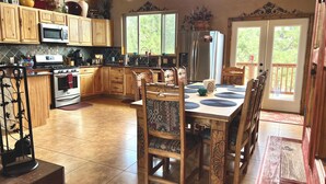 A spacious kitchen with wooden cabinets, a large island, and a dining area with a table and chairs. - Three Bears Cabin (Angel Fire)