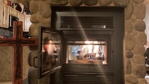A stone fireplace with a glass door, a wooden ceiling, and a rustic decor. - Three Bears Cabin (Angel Fire)