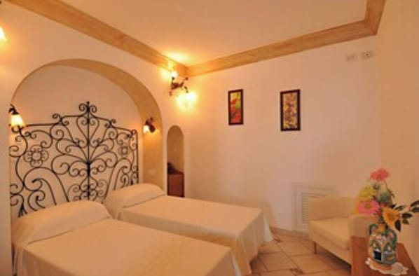 Una habitación con dos camas, techo de madera, radiador y un jarrón con flores.