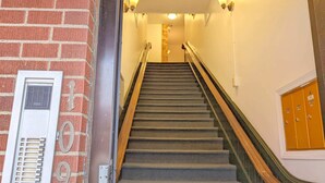 Eine Treppe mit Teppichstufen, einem Metallgeländer und einer Ziegelwand mit Lüftungsgitter und Nummernschild.